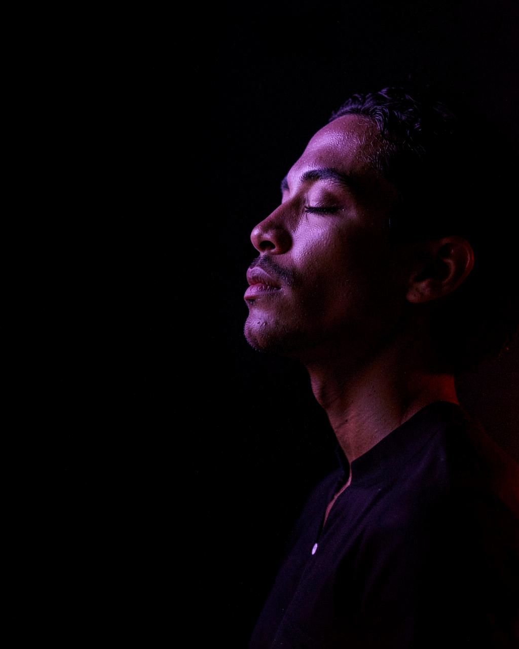 A person in profile, eyes closed, lit by violet and red light against darkness